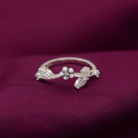 Elegant silver ring featuring floral design with white stones and sparkling accents on a deep burgundy fabric background.